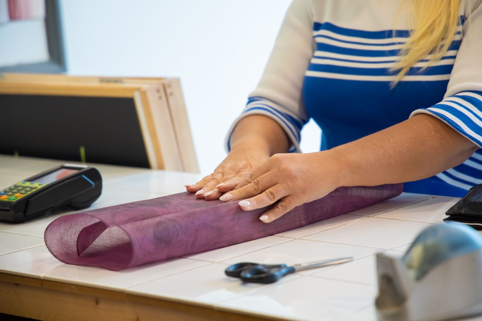A woman wraps a gift in purple tissue paper beside scissors and a card terminal.