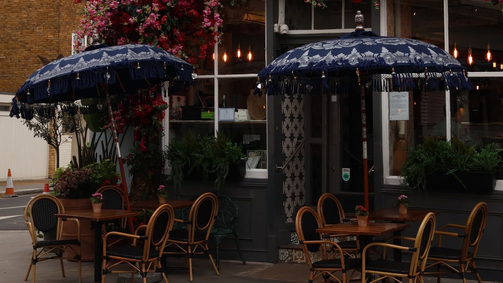 An outdoor café with blue umbrellas and tables beside a brick building in London, United Kingdom.