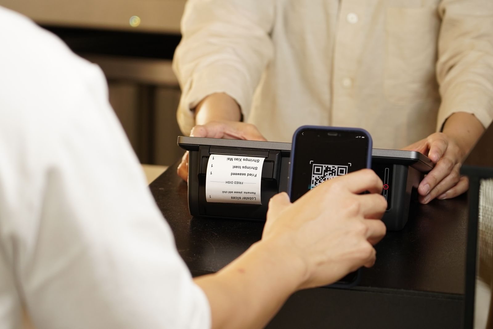 A smartphone and QR code scanner are used together at a retail counter.