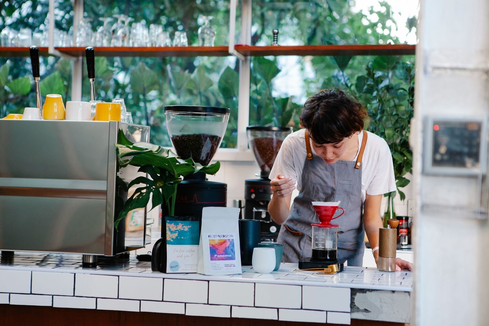 A barista preparing pour-over coffee behind a cafe counter.