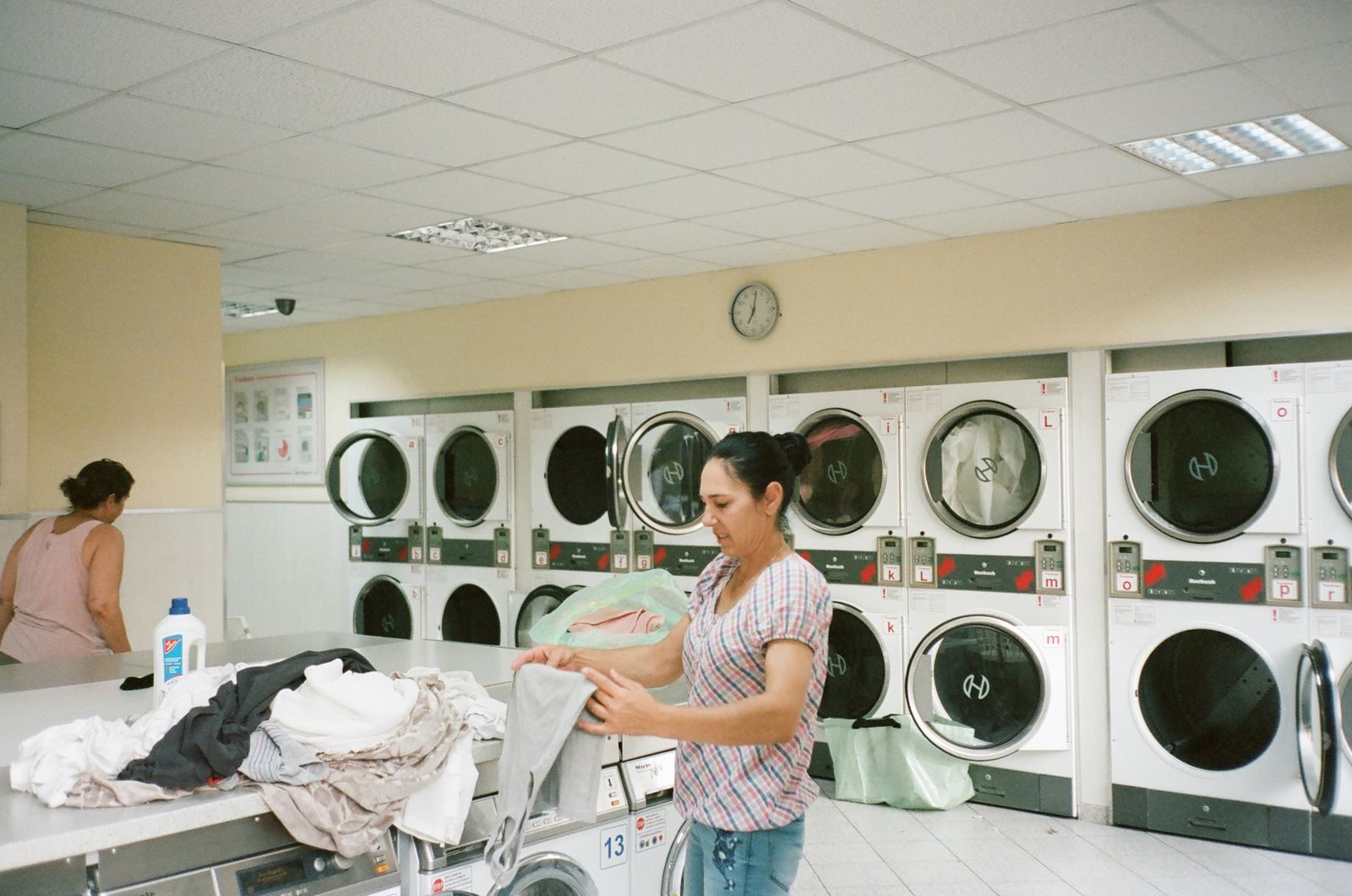 A woman folding clothes beside washing machines at a laundromat.